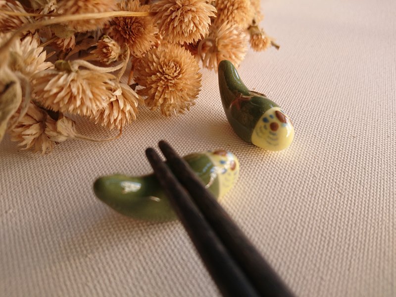 Hey! Bird friend! Green budgerigar lying on the chopstick rest
